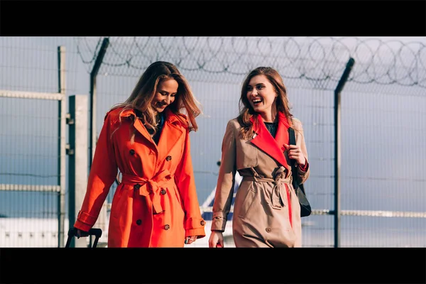Dos chicas felices caminando cerca del aeropuerto, con equipaje. Viajes aéreos, vacaciones de verano — Foto de Stock