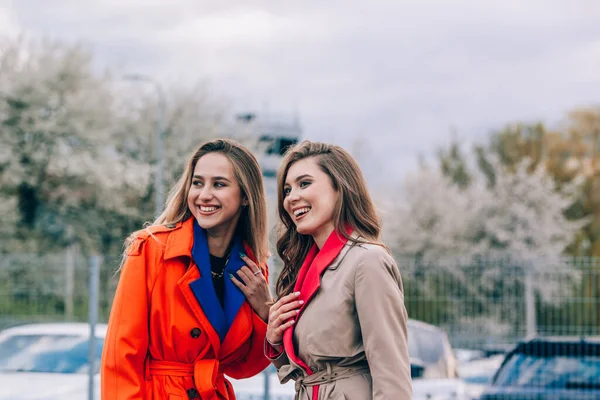 Mujer rubia sonriente feliz de moda con abrigo naranja, jeanse azul y cadena de cuello comunicarse con su novia en la calle. — Foto de Stock