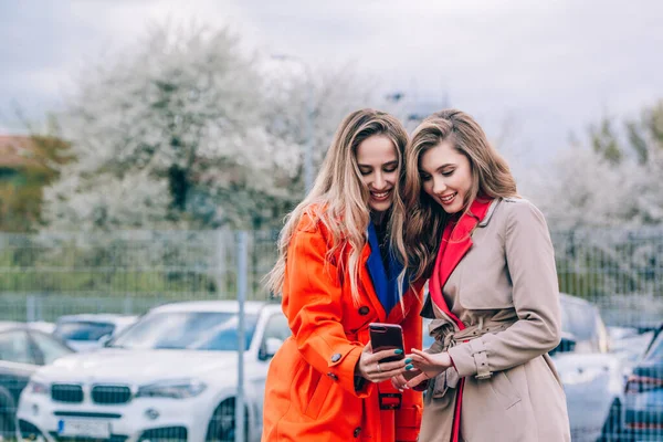 Mujer rubia sonriente feliz de moda con abrigo naranja, jeanse azul y cadena de cuello comunicarse con su novia en la calle. — Foto de Stock