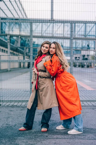 Mujer rubia sonriente feliz de moda con abrigo naranja, jeanse azul y cadena de cuello comunicarse con su novia en la calle. — Foto de Stock