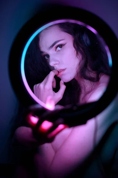 Эмоциональный студийный портрет молодой женщины в беспроводных наушниках с эффектом кольца вспышки. Круглая светодиодная лампа. — стоковое фото