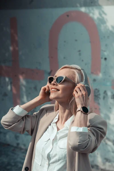 Retrato de mujer rubia en auriculares escuchando música con gafas de sol. Hipster modelo de moda llevar elegantes auriculares inalámbricos disfrutar escuchar nueva música fresca. — Foto de Stock