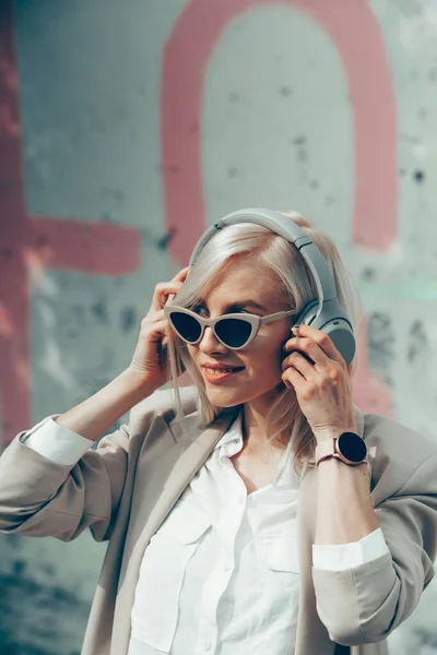 Portrait of blonde woman in headphones listening music with sunglasses. Hipster fashion model wear stylish wireless headphones enjoy listen new cool music. — Stock Photo, Image
