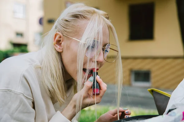 Young smiling hipster happy woman doing make-up using lipstick and mirror outdoors — Stock Photo, Image