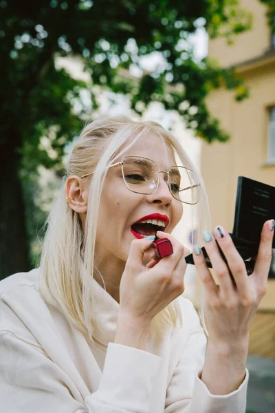 Joven sonriente hipster feliz mujer haciendo maquillaje usando lápiz labial y espejo al aire libre — Foto de Stock