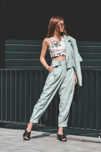 Modeportret van een jonge vrouw met een zonnebril, top, slingbacks, blauw pak. jong mooi gelukkig model poseren in de buurt grijs metalen rooster — Stockfoto