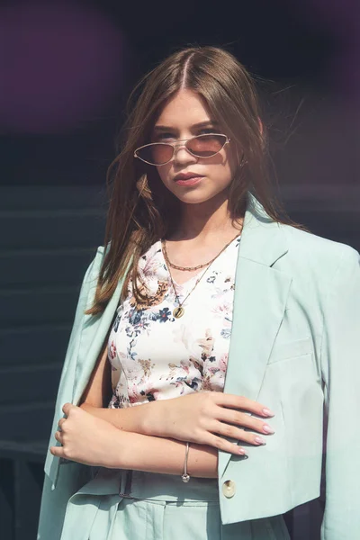 Güneş gözlüğü takan genç bir kadının moda portresi, üst ve mavi takım elbise. Genç, güzel, mutlu model, karanlık arka planda poz veriyor. — Stok fotoğraf