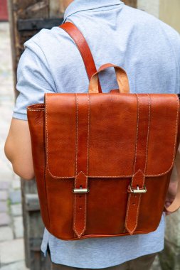 Deri sırt çantalı şık bir adam dışarıda yürüyor.