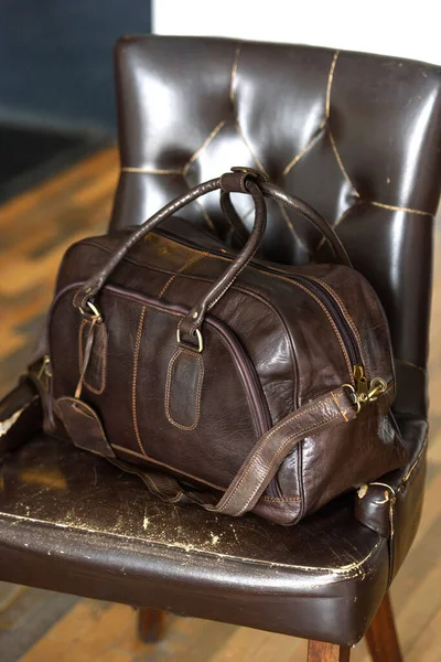 Leather brown travel bag, on a brown leather chair — Stock Photo, Image