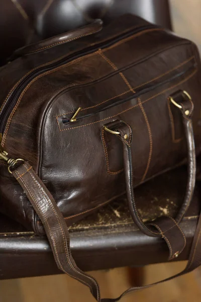 Leather brown travel bag, on a brown leather chair — Stock Photo, Image