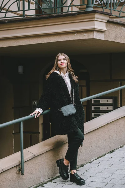 Foto de cerca de la joven hermosa mujer en abrigo de piel negro, jeanse y zapatos posando en la calle — Foto de Stock
