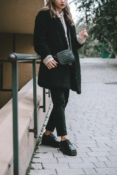 Крупный план фотографии молодой красивой женщины в черном шубе, джинсе и обуви, позирующей на улице — стоковое фото