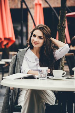 Kafe masasında oturan dizüstü bilgisayarını kullanan serbest çalışan genç bir kadın. İnternette çalışan gülümseyen kadın ya da not defteri kullanırken çalışıp öğrenen..