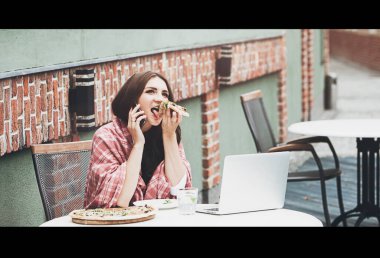 Genç serbest çalışan, kafede pizza yerken akıllı telefon kullanarak iletişim kuruyor.