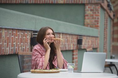 Genç serbest çalışan, kafede pizza yerken akıllı telefon kullanarak iletişim kuruyor.