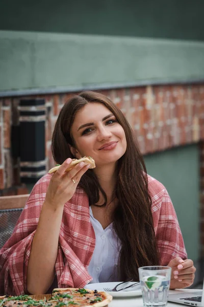 Rolig brunett flicka i en vit blus äter pizza på restaurang. Utomhus — Stockfoto