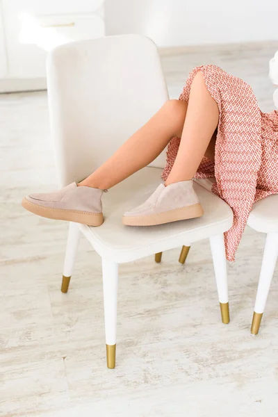 Bej etekli kadın bacakları ve şık süet mokasen mokasen. Arkaplanda hafif ahşap kaplama dokusu