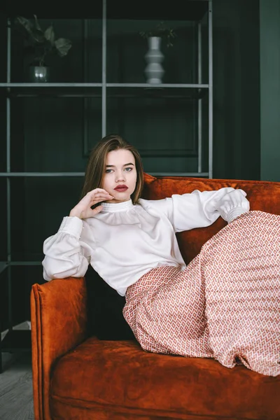 Retrato de mulher jovem na moda em uma saia bege e blusa branca posando em um sofá laranja. — Fotografia de Stock