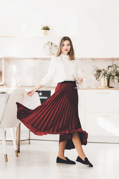 Portrait de femme à la mode en jupe rouge, chemisier blanc et élégantes chaussures en daim avec une boucle posant sur la cuisine. Fille avec un verre de vigne dans les mains — Photo