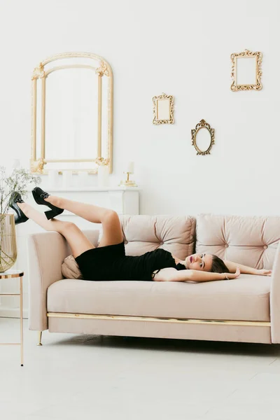 Foto av en kvinnas ben i svarta högklackade skor med ett spänne. Kvinnan poserar på en soffa — Stockfoto