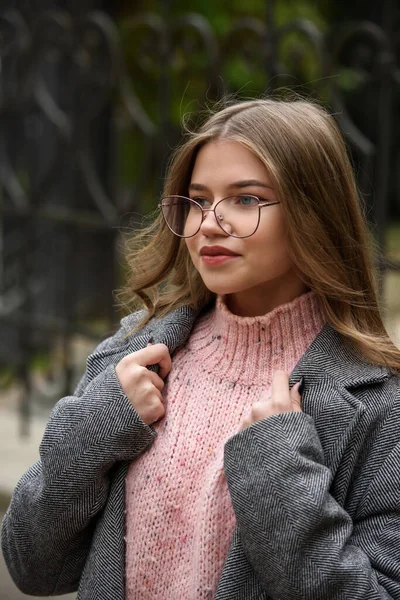 유행적 이고 아름다운 16-20 세 의젊은 아가씨 핑크 색 뜨개 질 스웨터, 안경, 검은 스커트, 회색 클래식 해구 코트를 입고. — 스톡 사진