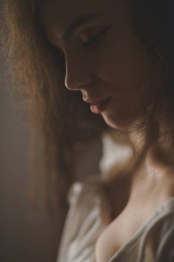 Stüdyoda baştan çıkarıcı pozlar veren uzun kıvırcık saçlı seksi genç bir kadının portresi.