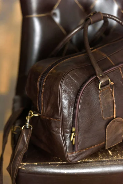 Leather brown travel bag, on a brown leather chair — Stock Photo, Image