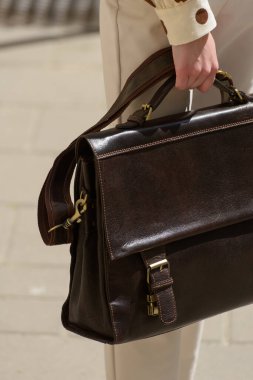 Part photo of a woman with a brown leather briefcase with antique and retro look. Outdoors photo