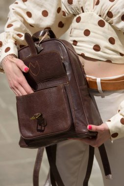 Part photo of a woman with a brown leather backpack with antique and retro look. Outdoors photo
