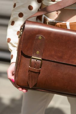 Part photo of a woman with a brown leather briefcase with antique and retro look. Outdoors photo