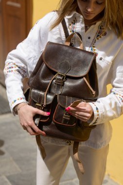 Antika ve antika görünümlü kahverengi deri sırt çantalı bir kadının resmi. Açık hava fotoğrafı.