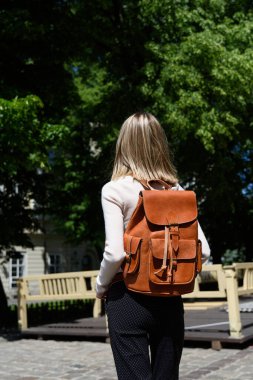 Antika ve antika görünümlü turuncu deri sırt çantalı bir kadın. Açık hava fotoğrafı..