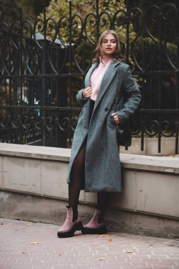 young beautiful girl posing on the autumn street. Dressed in a stylish gray coat, knitted pink sweater and skirt. small stylish handbag
