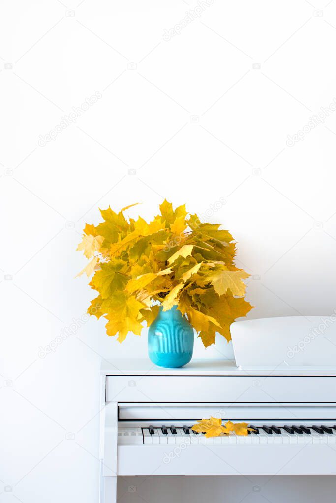 Maple leaves on the piano in a blue vase. The concept of autumn.