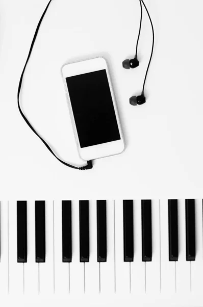 Клавиши фортепиано и устройство воспроизведения музыки с наушниками. Черно-белое фото. — стоковое фото