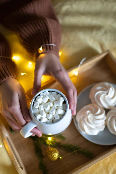 Une grande tasse avec du cacao dans les mains d'une fille, en arrière-plan de meringue et de lumières. — Photo