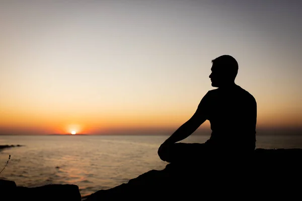 Чоловік насолоджується видом на захід сонця на море, сидячи на скелі . — стокове фото