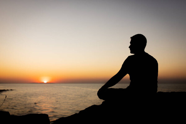 A man enjoys the view of the sunset on the sea, sitting on a rock.