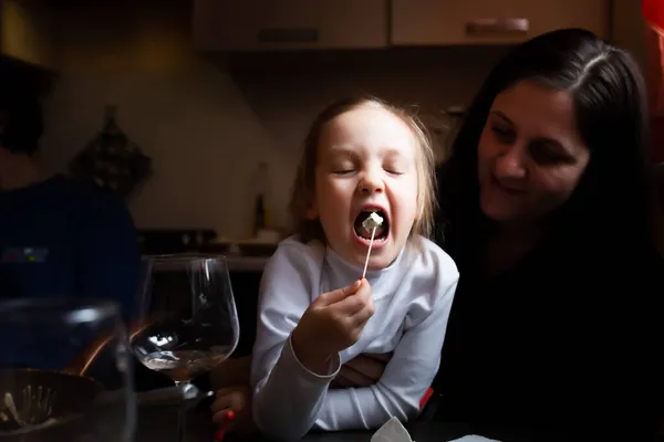 Das Mädchen isst Käse mit blauem Schimmel im Arm ihrer Mutter. — Stockfoto