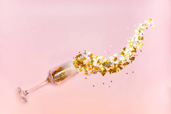 New Year card. Glass of champagne, gold sparkles pouring out of the glass on a pink background. — Stock Photo, Image