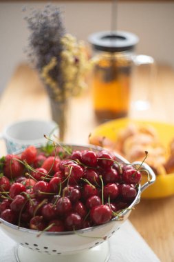 Yaz kahvaltısı, kiraz ve çilek kasede, çayla turtalar, çiçeklerle dolu masa..