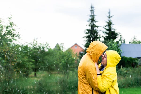 Sarı yağmurluklu evli bir çift arka bahçelerinde yağmurda. — Stok fotoğraf