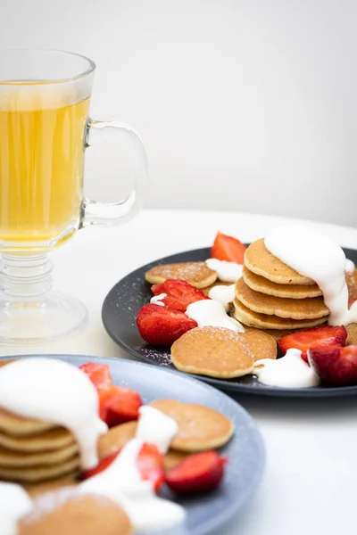 Mini pancakes with sour cream sauce and strawberries on plates, breakfast for the family. — Stock Photo, Image
