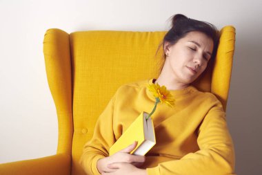 Sandalyesinde kitap ve çiçekle uyuyan güzel bir kadın..