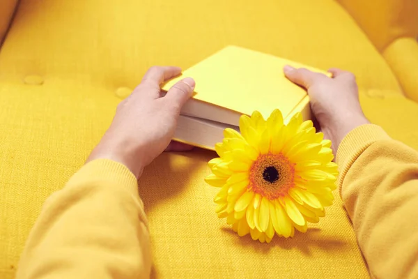 Elinde bir kitap olan sarı bir sandalye ve içinde bir çiçek var.. — Stok fotoğraf