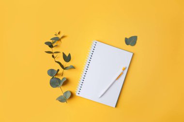 Okaliptüs yaprakları ve sarı arka planda bir kalemle birlikte bir defter. Metin ve metin boşluğu için yer.