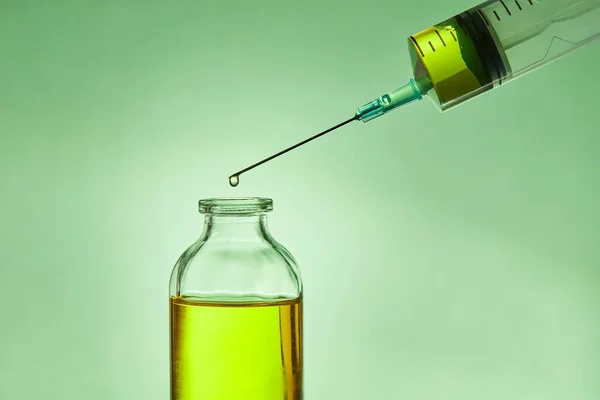 A drop of liquid drips from the needle of a medical syringe into the bottle. — Stock Photo, Image