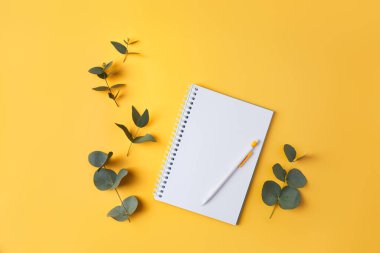 Okaliptüs yaprakları ve sarı arka planda bir kalemle birlikte bir defter. Metin ve metin boşluğu için yer.