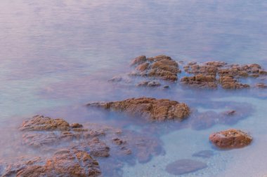 Deniz kıyısındaki kayalar parlak turkuaz suyla neşeli görünür ve deniz ya da deniz yaşamı, çizgi film ya da doğa için arka plan görüntüsü olarak kullanılabilir..