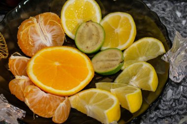 Turunçgil meyveli kaplama. Tabakta limon, portakal, feijoa ve mandalina dilimleri var. Yıldızlar ve kalpler şeklinde çelenklerle dolu parlak bir hayat. Örgü bir eşarbın üzerinde duruyor, bu da fotoğrafa özel bir ruh hali veriyor..